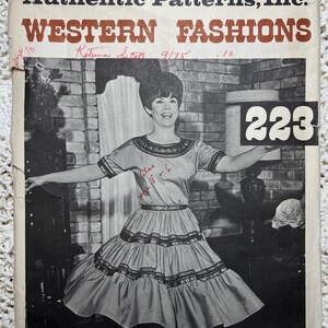 May include: Vintage sewing pattern cover with the text "Authentic Patterns, Inc. WESTERN FASHIONS". The cover features a black and white photo of a woman in a dress, holding a sign with the number 223.