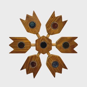 May include: A wooden snowflake-shaped decorative item. The item is made of light brown wood with six pointed sections, each containing a small, round, colored stone. The center and the stone in each section are dark.