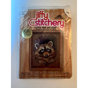 May include: A Jiffy Stitchery embroidery kit titled Little Tree Raccoon designed by Andree Palmateer. The packaging features a raccoon graphic, fits a 4 inch by 5 inch Jiffy Frame, and includes printed homespun fabric, wool yarn, needle, and mounting board.
