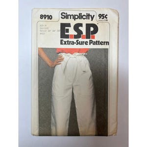 May include: A Simplicity 8910 sewing pattern envelope for E.S.P. Extra-Sure Pattern. The front features a photograph of white trousers with a high, gathered paper-bag waist, a tie belt, and large patch pockets. The text includes size H 6, 8, 10.