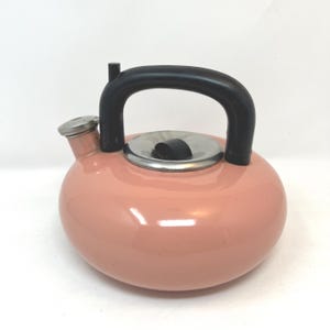 May include: A pink, round tea kettle with a black handle and spout. The kettle has a silver lid and spout cap. The handle is arched, and the spout is short and angled. The kettle is made of metal and has a glossy finish.