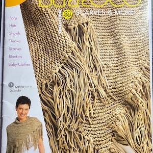 May include: A magazine cover featuring a knitted shawl with fringe. The cover has the text "BERROCO SCARVES & MORE" and lists items like scarves, shawls, and blankets. The image also shows a woman wearing a similar shawl.