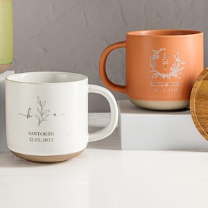 Può includere: Quattro tazze in ceramica verde, arancione e bianca, con sottobicchieri in legno abbinati. Le tazze e i sottobicchieri presentano disegni personalizzati, tra cui iniziali, elementi floreali e date. I sottobicchieri sono rotondi e le tazze hanno manici.
