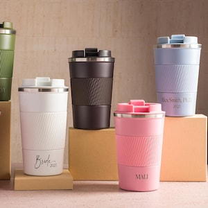 May include: An assortment of insulated travel mugs in colours such as black, green, red, white, brown, pink, and lavender. Each mug features a ribbed silicone sleeve and a stainless steel lid. Some mugs have personalized text.