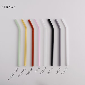 Pu&ograve; includere: Una collezione di otto cannucce in vetro piegate disposte in fila, etichettate BENT STRAWS. I colori includono verde giada chiaro, giallo, ambra, rosa, trasparente, nero, grigio e bianco. Ogni cannuccia presenta una piegatura angolata.