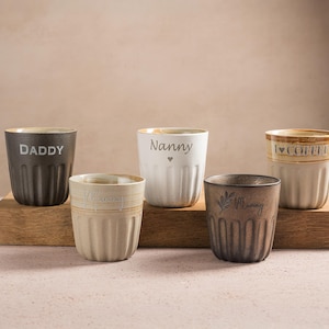 May include: A trio of ceramic mugs with a speckled, matte finish in cream, light grey, and dark grey. The mugs have a simple, minimalist design, ideal for tea or coffee.