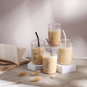 May include: Four clear glass cups with lids and straws, each filled with a light brown beverage. The cups are labelled with the words "Coffee", "Sugar", "Espresso", and "Kiss".