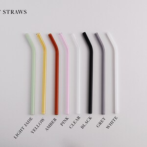 Pu&ograve; includere: Una collezione di otto cannucce in vetro piegate disposte in fila, etichettate BENT STRAWS. I colori includono verde giada chiaro, giallo, ambra, rosa, trasparente, nero, grigio e bianco. Ogni cannuccia presenta una piegatura angolata.
