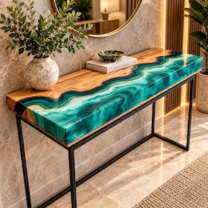 May include: A rectangular console table featuring a natural wood slab top with a flowing, marbled teal and green resin inlay. The table is supported by a thin, black metal frame. A textured ceramic vase and a book are placed on the surface.