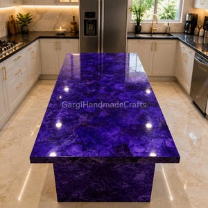 Può includere: Un'isola cucina rettangolare con un piano di lavoro in pietra preziosa viola intenso lucido, caratterizzato da una texture cristallina naturale. La superficie presenta varie tonalità di viola e indaco con riflessi. Testo: GargiHandmadeCrafts.
