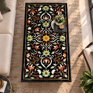 Pode incluir: Uma mesa de centro retangular com uma superfície preta apresentando um intrincado padrão floral incrustado em tons de laranja, amarelo, branco e verde claro. O tampo da mesa exibe um design botânico simétrico com vinhas e flores.