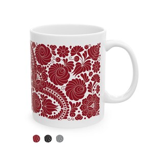 May include: White ceramic mug featuring a detailed floral pattern in burgundy. The design includes stylized flowers, leaves, and swirling elements. The mug has a curved handle and a glossy finish, suitable for hot beverages.