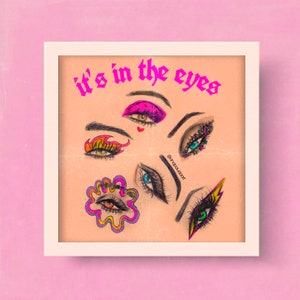 May include: A framed print with the text "it's in the eyes" in pink letters. The print features a collage of colorful eyes with different makeup styles.