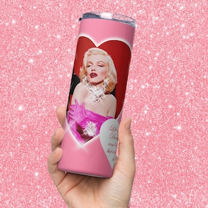 Puede incluir: Un vaso rosa de acero inoxidable con un diseño en forma de corazón con un retrato de Marilyn Monroe. El vaso tiene una tapa rosa y una cita que dice "Life is a Dream and it is beautiful".