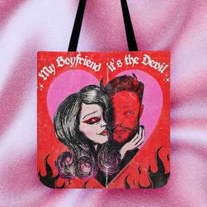 Op de afbeelding: Rode tote bag met zwarte handvatten. Het ontwerp toont een illustratie in vintage stijl van een stel met duivelse kenmerken in een roze hart, met de tekst "My Boyfriend it's the Devil". Vlammen en sterren omringen het hart.