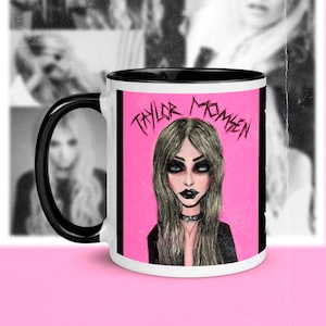 May include: White ceramic mug with a black rim and handle. The mug features a pink background with a black and white illustration of a woman with dark hair and dark makeup. The text "Taylor Momsen" is written in black across the top of the image.