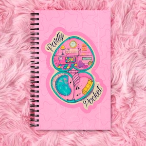 May include: Pink spiral bound notebook featuring a pink and blue illustration of a heart-shaped compact with the words "Party Pocket" on it. The background is a pink pattern of stars.