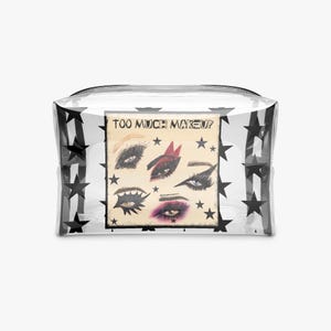 Puede incluir: Un neceser transparente con detalles de estrellas negras y un inserto rectangular con ilustraciones de maquillaje de ojos. El inserto tiene el texto "TOO MUCH MAKEUP".