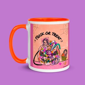 Puede incluir: Una taza de cerámica blanca con un borde naranja. La taza presenta una ilustración colorida de una calabaza llena de caramelos y el texto "Trick or Treat".
