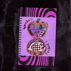 May include: A purple notebook with a spiral binding features a black and white illustration of a spooky pocket-sized house with a chequered floor and a green tree. The text "Spooky Pocket" is written in a pink font with stars.