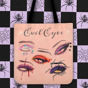 Puede incluir: Una bolsa de tela rosa con el texto "Evil Eyes" y cuatro ilustraciones de ojos diferentes. Los ojos están dibujados en un estilo de dibujos animados con maquillaje colorido y purpurina. El fondo es un patrón de cuadros con telarañas.