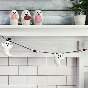 May include: A black and white ghost garland with pink and black beads hanging on a white tiled fireplace mantel.