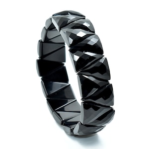 May include: A black bracelet with geometric, faceted links. The bracelet is made of a shiny, dark material and is set against a white background. The links are triangular and square-shaped.