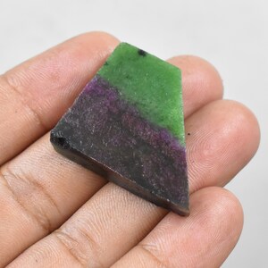 Pode incluir: Uma pedra preciosa com um padrão de cores único. A seção superior é verde, seguida por uma faixa roxa e uma base cinza escura. A pedra tem uma forma geométrica e uma superfície polida. Esta pedra natural é ideal para fazer joias.