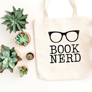 May include: A white canvas tote bag with black text that reads "BOOK NERD" and a pair of black glasses graphic.