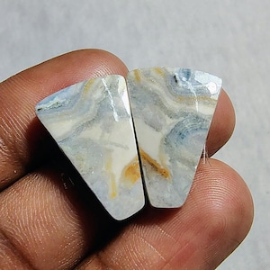 May include: Two blue, white, and gold agate cabochons with a triangular shape. The cabochons have a swirling pattern.