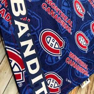 May include: A blue fabric with a pattern of the Montreal Canadiens logo and text. The text "MONTREAL CANADIENS" is in red and white. The word "BANDIT" is printed vertically in white. The fabric has a stitched red border.