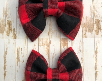 May include: Two red and black plaid fabric hair bows. The bows are tied in a classic bow shape.