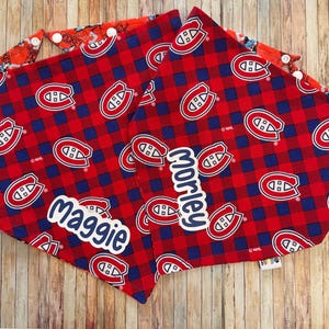May include: Red and blue plaid dog bandanas with the Montreal Canadiens logo. One bandana has the name "Maggie" and the other has "Morley" in white script. The bandanas have snap closures.