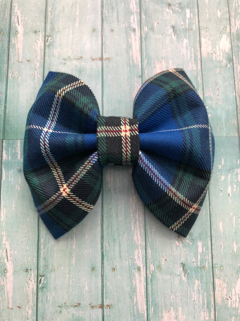 May include: A large, fabric bow in a classic plaid pattern. The bow features a combination of blue, green, and white lines, with a touch of red. The bow is centered with a matching fabric piece. The bow is a hair accessory.