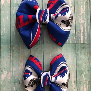 May include: Two blue and red fabric hair bows with a white buffalo logo and the word "Bills" printed on them.