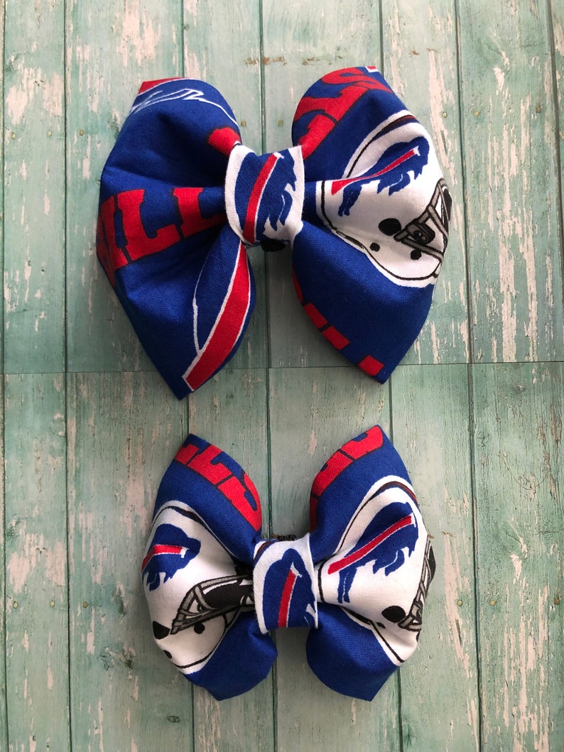 May include: Two blue and red fabric hair bows with a white buffalo logo and the word "Bills" printed on them.