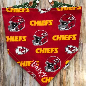 May include: Red and yellow bandana with a football helmet and "CHIEFS" repeated on the fabric. The bandana is personalized with the name "Daisy" in white cursive.