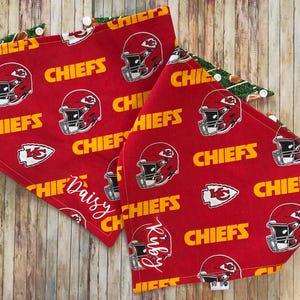 May include: Two red and yellow fabric dog bandanas with a Kansas City Chiefs pattern. One bandana says "Daisy" and the other says "Riley".