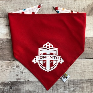May include: Red dog bandana featuring a white Toronto FC logo. The bandana has a white reverse side with colourful paw prints.