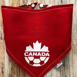 May include: Red bandana with a white football and the word "CANADA" printed on it. The bandana has white poppers on the top.