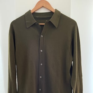 May include: A long-sleeved, button-up shirt in a dark green colour. The shirt has a collared neckline and a relaxed fit.