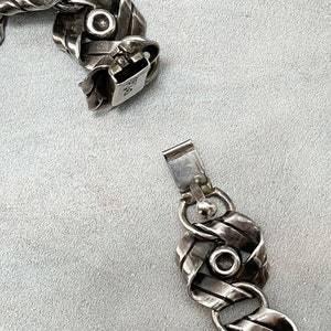 K&ouml;nnte beinhalten: Ein silbernes Armband mit geflochtenem Design und einem Verschluss. Das Armband besteht aus mehreren Silberstr&auml;ngen, die miteinander verflochten sind, um ein einzigartiges und kompliziertes Design zu schaffen. Der Verschluss ist einfach, aber sicher, so dass das Armband leicht an- und ausgezogen werden kann.