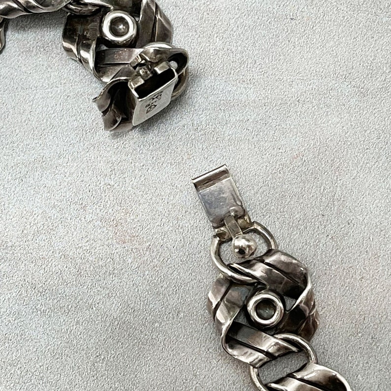 K&ouml;nnte beinhalten: Ein silbernes Armband mit geflochtenem Design und einem Verschluss. Das Armband besteht aus mehreren Silberstr&auml;ngen, die miteinander verflochten sind, um ein einzigartiges und kompliziertes Design zu schaffen. Der Verschluss ist einfach, aber sicher, so dass das Armband leicht an- und ausgezogen werden kann.