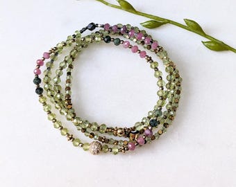 Könnte beinhalten: Ein mehrreihiges Armband mit grünen, rosa und schwarzen Perlen. Das Armband besteht aus kleinen, runden Perlen und hat eine goldene Akzentperle.