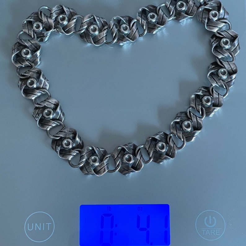 K&ouml;nnte beinhalten: Eine silberne Kettenkette mit geflochtenem Design und kleinen runden Akzenten. Die Kette liegt auf einer digitalen Waage, die 0,41 oz anzeigt.