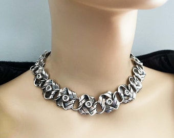 May include: A silver necklace with a woven chain design. The chain is made of thick, textured silver and has a series of round, silver accents.