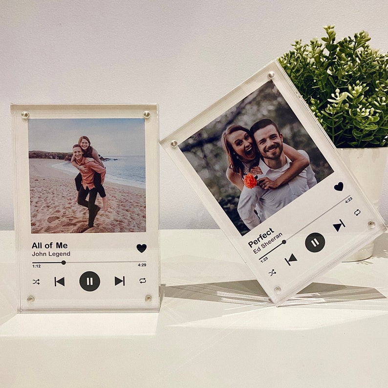 Pu&ograve; includere: Due blocchi fotografici in acrilico trasparente con foto e grafica del lettore musicale. Uno mostra una coppia su una spiaggia con "All of Me" di John Legend. L'altro mostra una coppia con "Perfect" di Ed Sheeran.