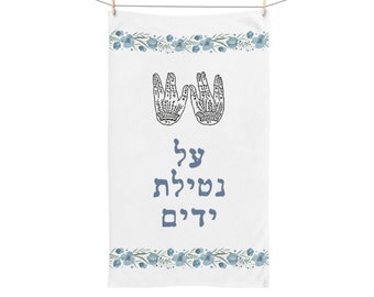 May include: White kitchen towel with a blue floral border and two stylized hands with Hebrew text that reads "Day of Blessing" in blue.