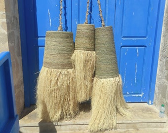 May include: Three woven baskets with long, light brown tassels hanging from a blue door. The baskets are made of natural materials and have a rustic, handmade look.