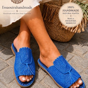 May include: Bright blue raffia sandals with a woven pattern and a tassel. The sandals are handmade in Essaouira, Morocco, and have a scalloped edge. The image also shows a raffia bag and the text "Essaouirahandmade".
